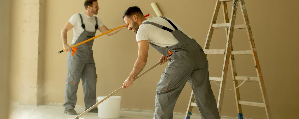 Deux peintres en fin de chantier : mur peint et sol en cours de nettoyage