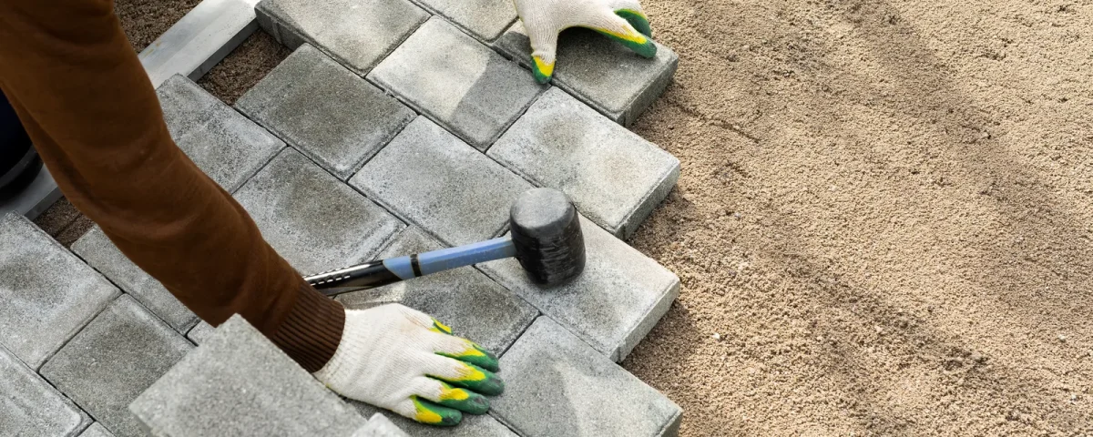 Pose de pavés béton sur lit de sable, maillet et mètre à proximité